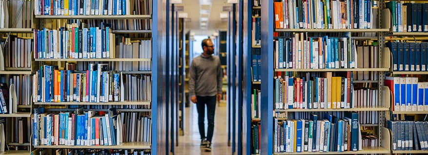 Student walking in between rows of books at the library